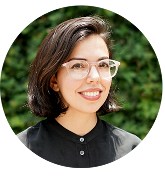 photograph of Raquel with light pink glasses, short brown hair, smiling in front of leaves